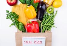 Paper grocery bag filled with vegetables and meal plan label.